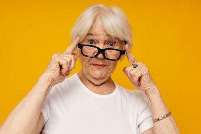 Portrait of senior woman holding eyeglasses against yellow background
