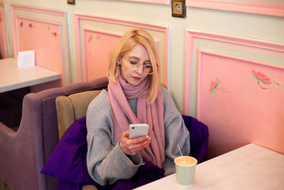 Young blonde woman in cafe drinks coffee and communicates on a smartphone