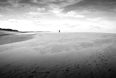 Distant view of person standing on sand against sky