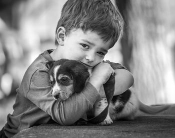 Portrait of cute boy embracing puppy on table while standing outdoors