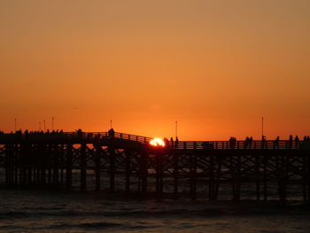 Silhouette pier over sea against orange sky
