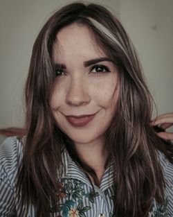 Portrait of smiling young woman with highlights on long hair against wall