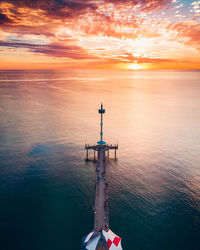 High angle view of people on pier over sea against orange sky