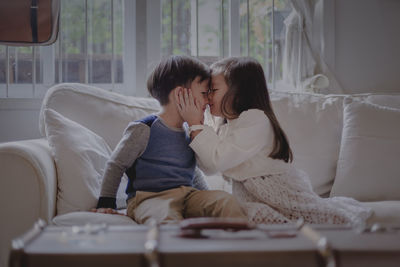 Cute siblings sitting on sofa at home