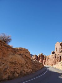 Road amidst rocks against clear blue sky