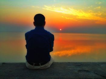 Rear view of silhouette boy standing at beach during sunset