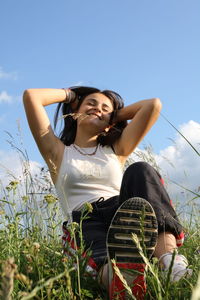 Low angle view of smiling girl sitting on land against sky