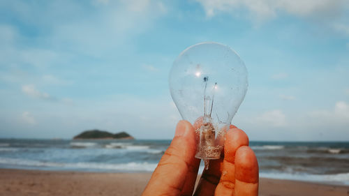 Close-up of hand holding damaged light bulb at beach
