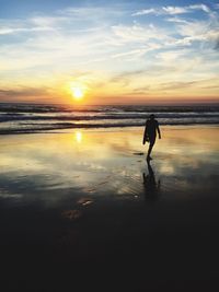 Silhouette man walking at beach against sky during sunset