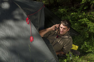 High angle view of man talking on phone while resting in tent at campsite