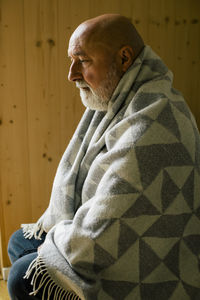 Thoughtful mature man wrapped in blanket sitting at home