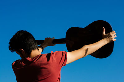 Rear view of shirtless boy holding blue sky against the background