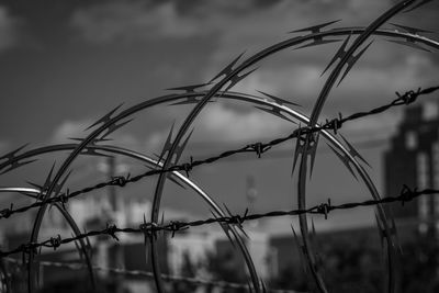 Low angle view of razor wire and barbed wire fence against sky