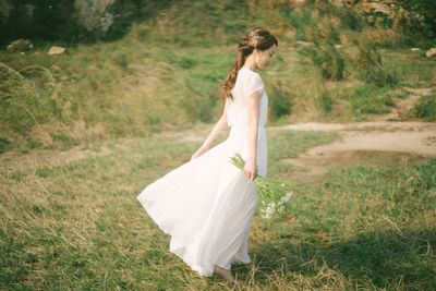 Side view of woman holding flowers while standing on grassy field