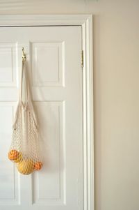 Mesh grocery bag, with variety of citrus inside, hanging on white door at home.