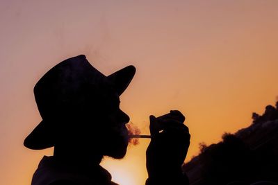 Silhouette man holding orange against sky during sunset