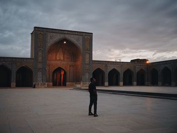 Man standing in front of historical building against cloudy sky