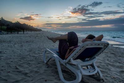 Deck chairs on beach against sky during sunset