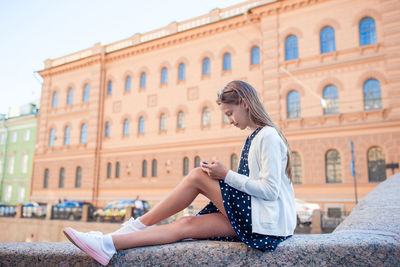 Side view of woman sitting against built structure