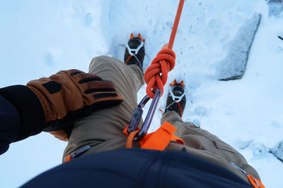 Low section of man standing on snow with safety harness and rope