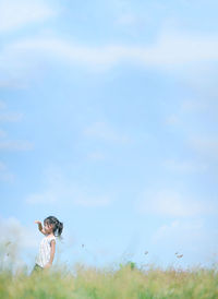 Side view of girl shielding eyes while standing on grassy field against sky