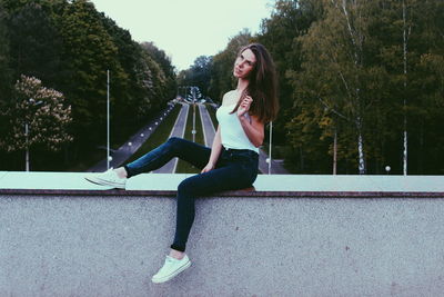 Portrait of young woman sitting on retaining wall