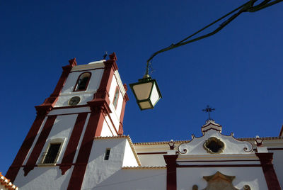 An old church in a portuguese town, with a street electric lamp in the foreground, against blue sky