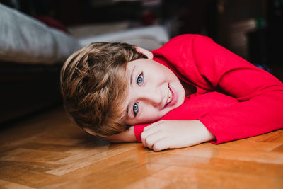 Portrait of smiling boy lying on hardwood floor at home