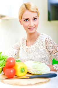 Portrait of young woman with vegetables on table at home
