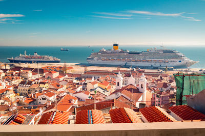 Modern ships moored in lisbon cruise port near houses with red tiled roofs against blue sky on sunny day in portugal