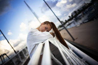 Portrait of woman leaning on railing against sky