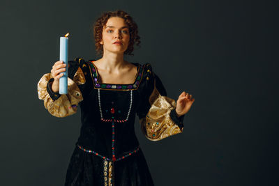 Portrait of young woman standing against black background