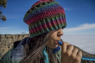 Close-up of woman in knit hat drinking against sky