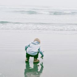 Rear view of boy crouching at beach