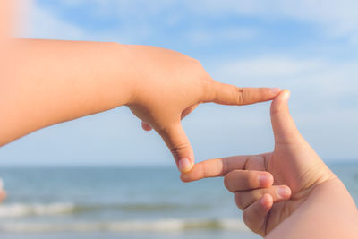 Cropped hands of child making finger frame against sea