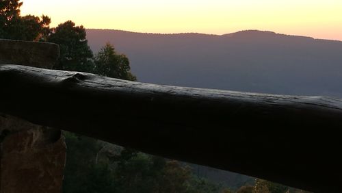 Close-up of railing by mountain against sky during sunset