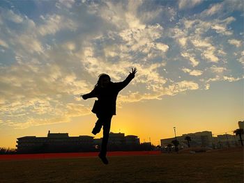 Silhouette man standing in city against sky during sunset