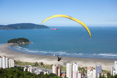 Person paragliding over buildings against beach
