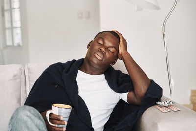 Man holding coffee cup while sleeping on sofa