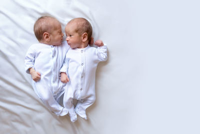 Newborn twins on the bed, in the arms of their parents, on a white background. emotions of kids.