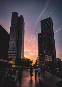 People on street amidst buildings against sky during sunset