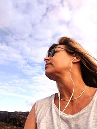 Low angle view of woman wearing in-ear headphones against cloudy sky