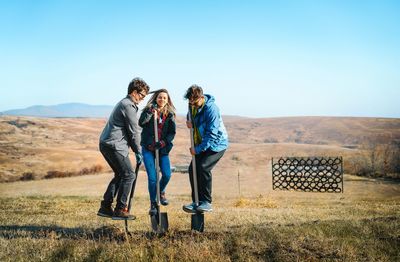 Full length of men and woman with shovels having fun on autumn field against clear blue sky 