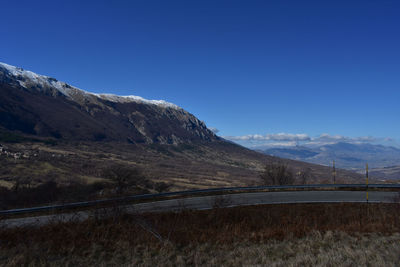 Road leading towards mountains against clear blue sky