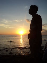 Side view of silhouette man standing at beach against sky during sunset