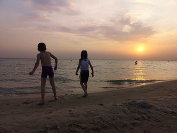 Rear view of men on beach against sky during sunset