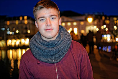Portrait of young man against illuminated city at night