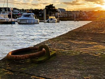 Boats moored on river by city against sky during sunset