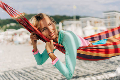 Young smiling tanned european woman relaxing in a hammock on the beach in summer.