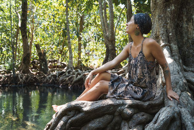 Young woman sitting on tree trunk in forest